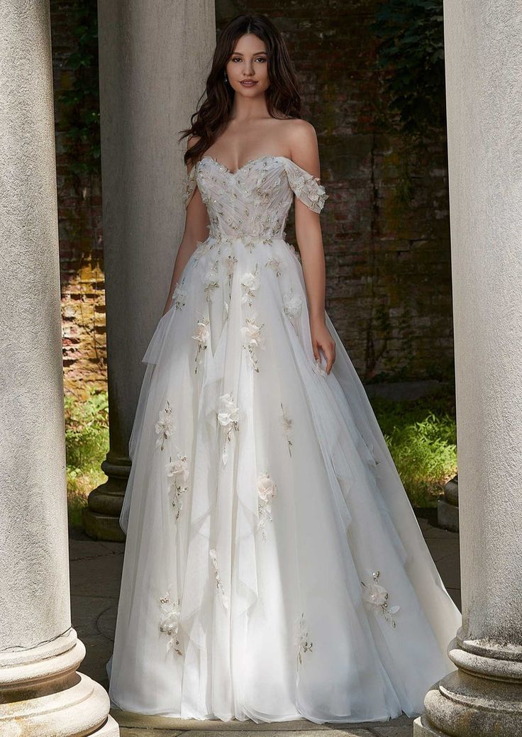 a woman in a white wedding dress standing under some pillars with her hands on her hips