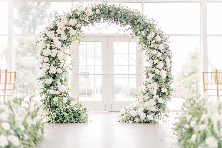 an archway decorated with white flowers and greenery at the end of a wedding ceremony