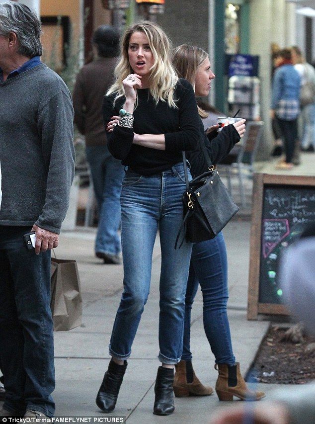 a woman is standing on the sidewalk talking to another person while others are walking by