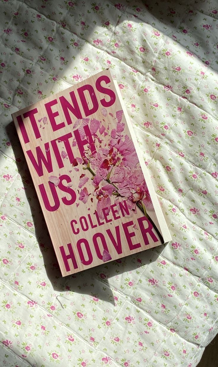 a book sitting on top of a bed covered in pink and white flowers with the title, it ends with us