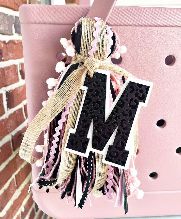 the letter m is attached to a pink chair with tassels and ribbons on it