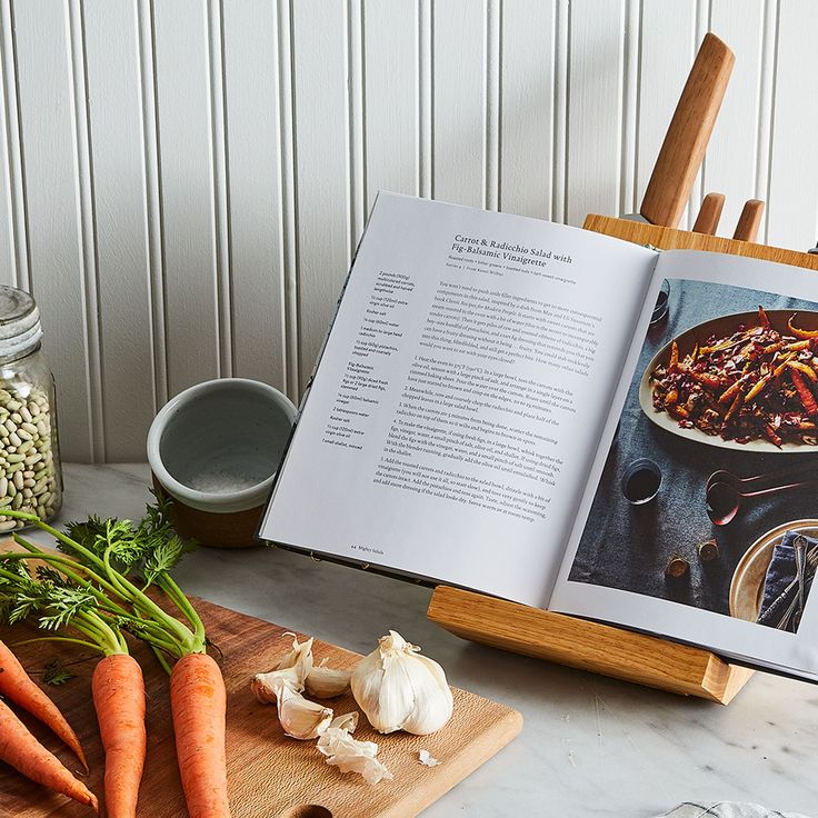 an open book sitting on top of a wooden cutting board next to carrots and garlic