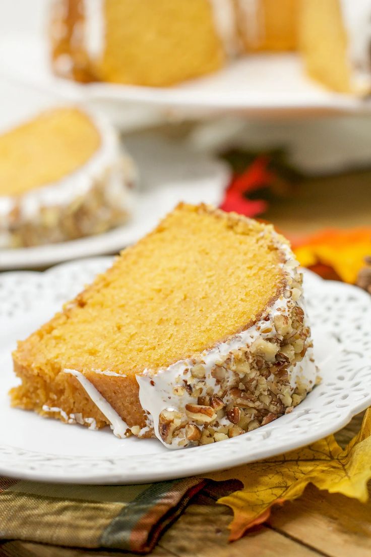 a slice of cake on a white plate with autumn leaves around it and another piece in the background