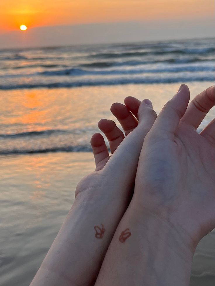 two hands holding each other with the sun setting in the background and water behind them