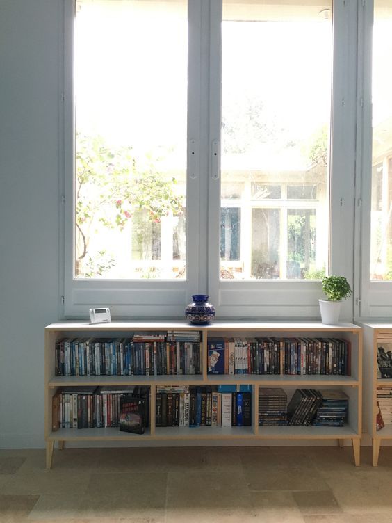 a bookshelf filled with lots of books next to two windows