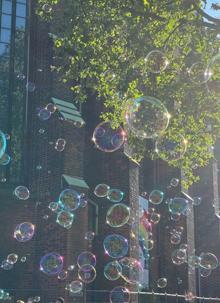 soap bubbles are floating in the air near a brick building and green trees on a sunny day