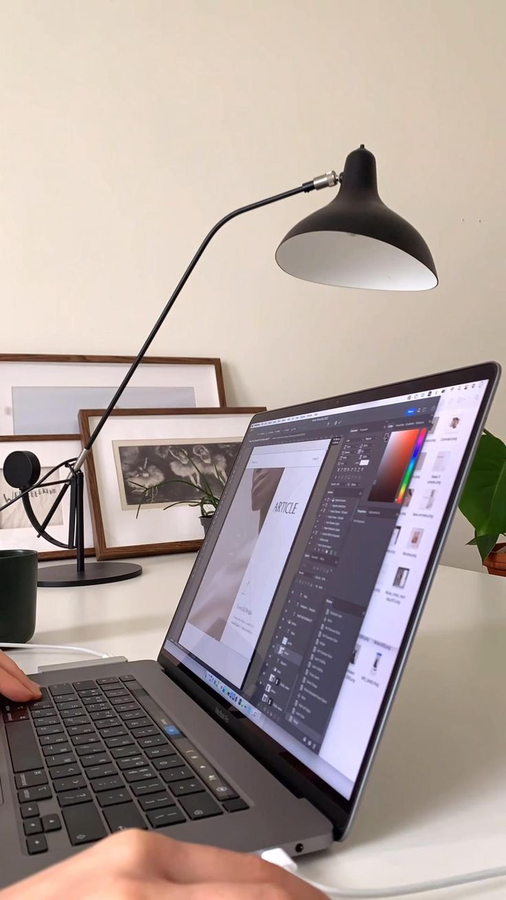 a person using a laptop computer on a white desk in front of a black lamp