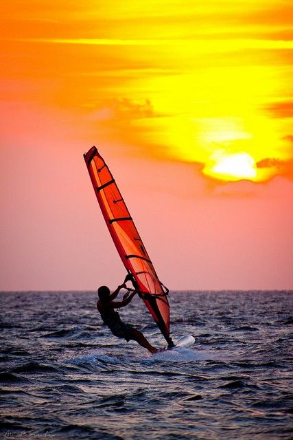 a person windsurfing in the ocean at sunset with an orange and red sail