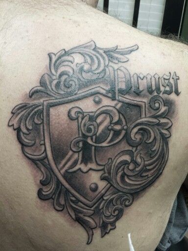 the back of a man's shoulder with a crest and cross tattoo on it