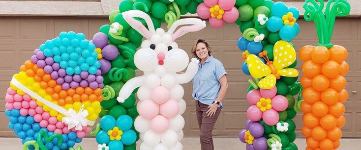 a woman standing in front of an arch made out of balloons with a bunny on it