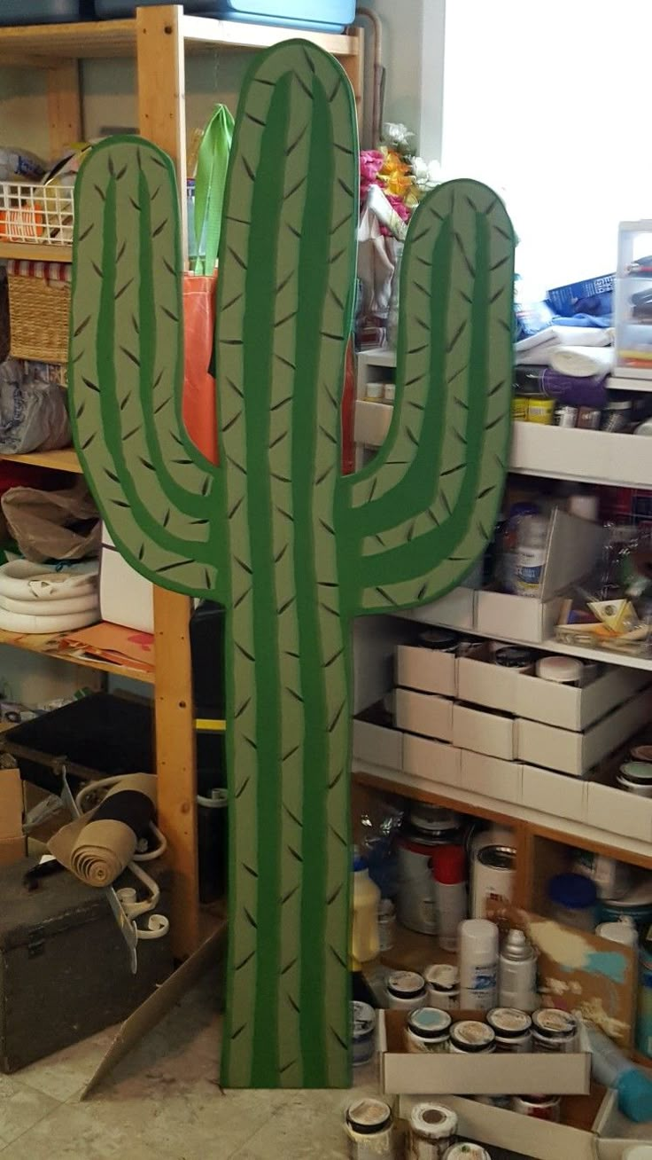 a large green cactus standing next to a shelf filled with paint and other items in a room