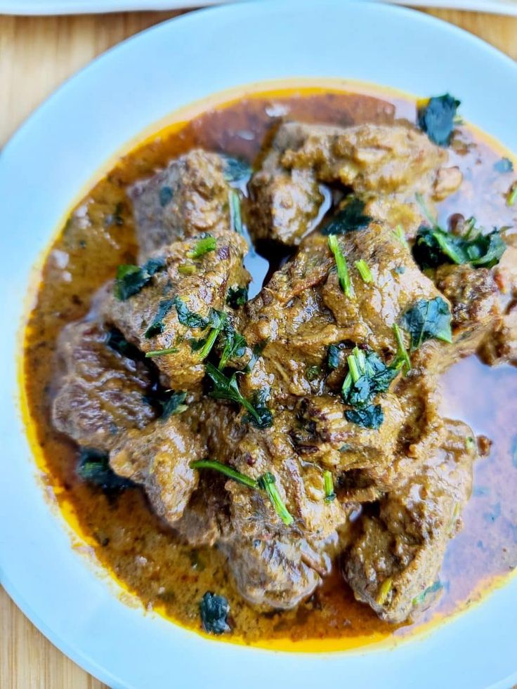 a white plate topped with meat covered in gravy and garnished with green leaves