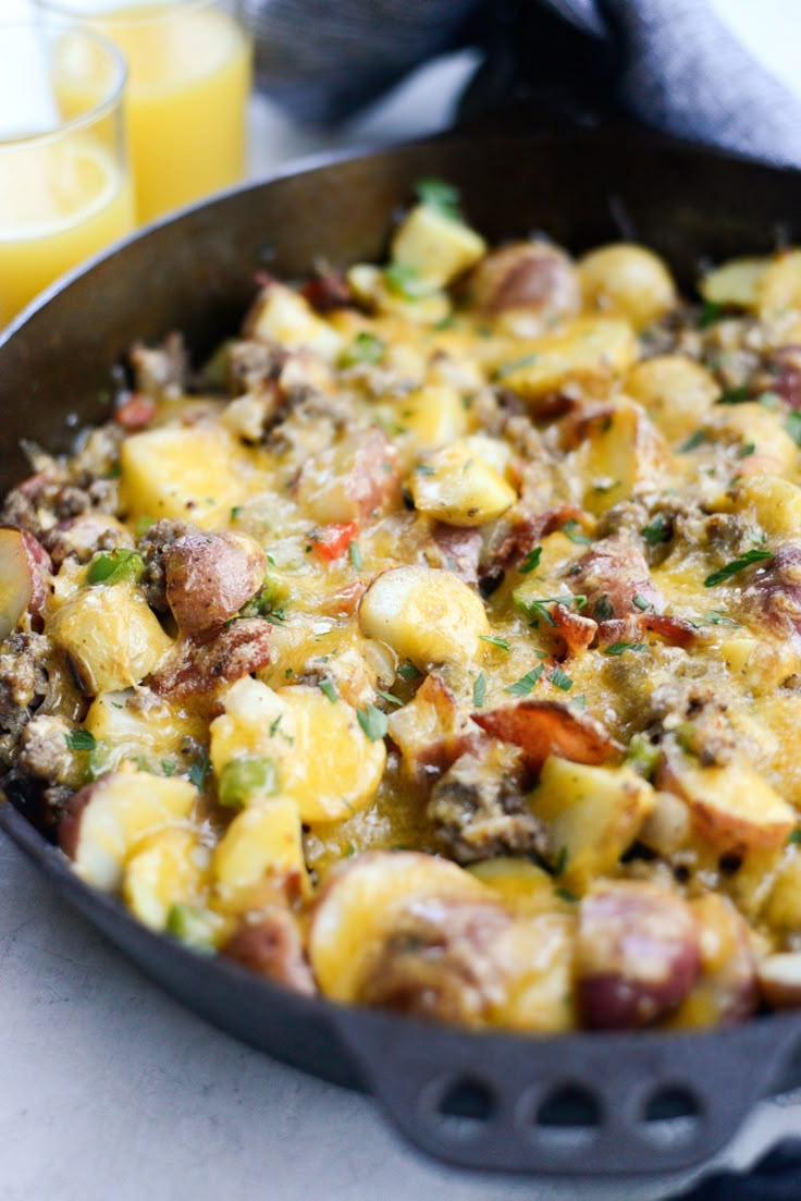 a skillet filled with potatoes and sausage next to orange juice in a glass cup