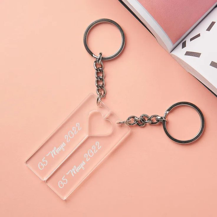 two clear acrylic keychains on a pink background with a book and pen