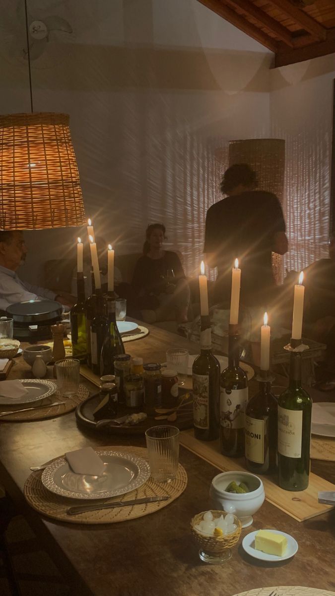 people sitting at a table with wine bottles and plates in front of them, surrounded by candles