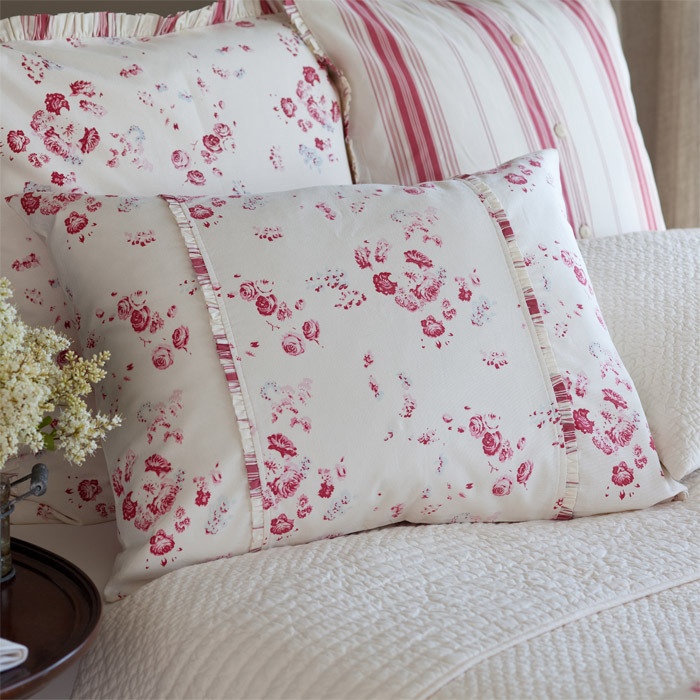 a bed topped with lots of pillows next to a vase filled with white and red flowers