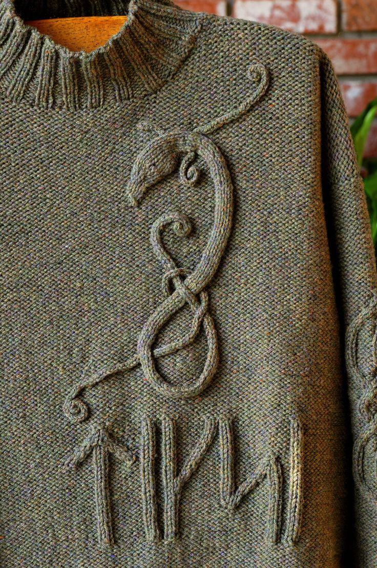 a close up of a sweater on a hanger next to a brick wall and green plants