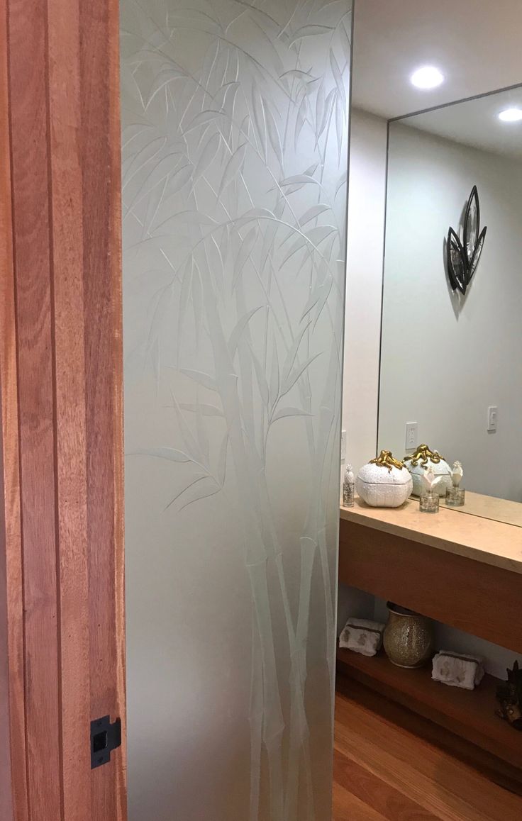 a bathroom with wood floors and a glass door that has trees etched on the side