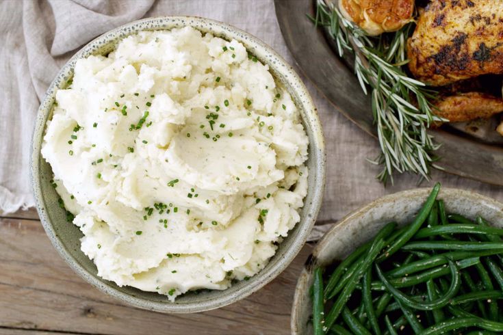 two bowls filled with mashed potatoes and green beans on top of a wooden table