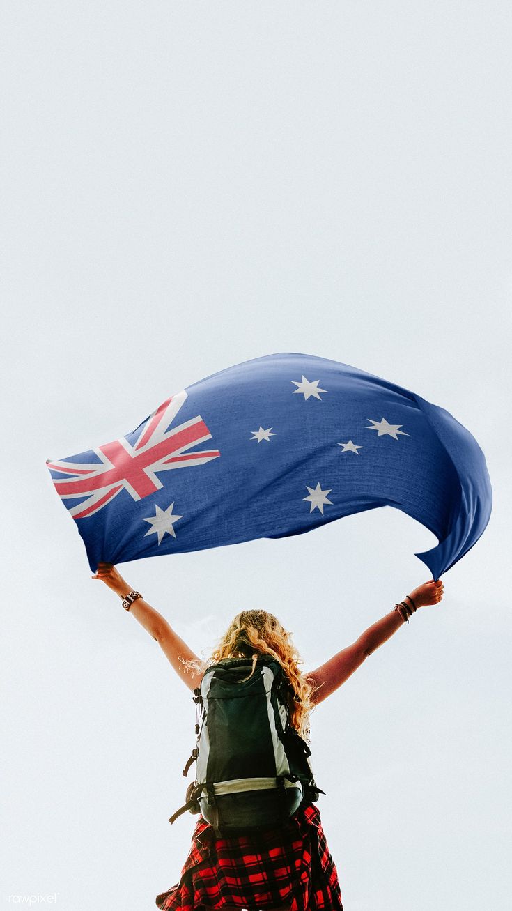 a woman holding an australian flag while standing on top of a hill with her hands in the air