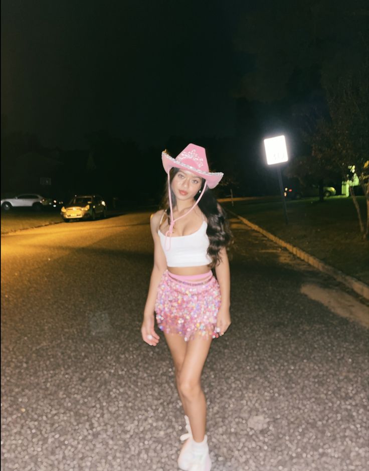 a girl wearing a pink cowboy hat standing in the middle of a road at night