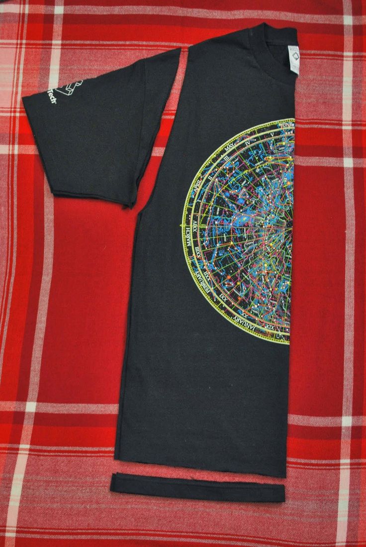 a black t - shirt with an abstract design on the front and back, sitting on a red plaid blanket