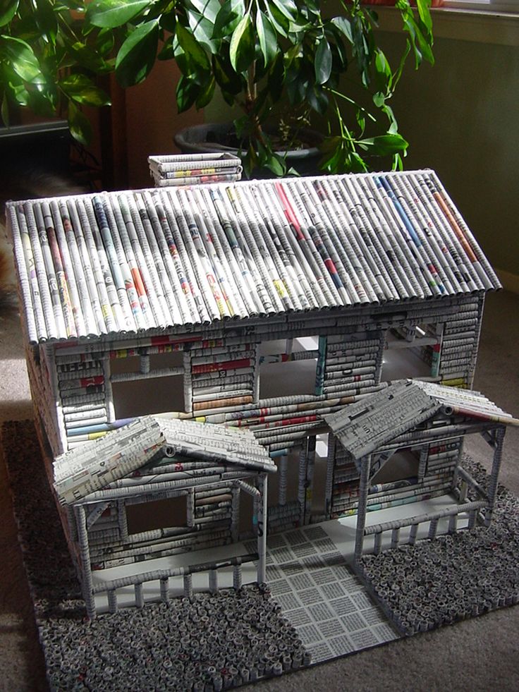 a house made out of magazines sitting on top of a rug next to a potted plant