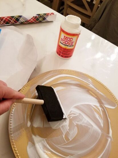 a person is painting a plate with white paint and a brush on it while another hand holds a wooden spatula