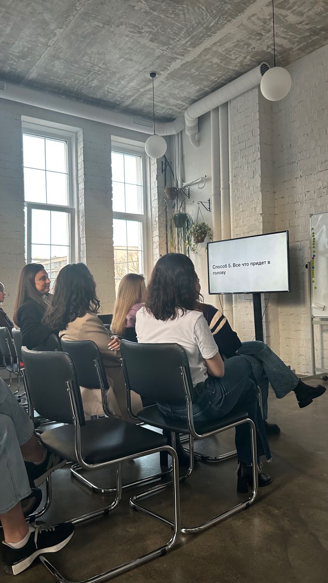 group of people sitting in chairs listening to a presentation on a projector screen at an office