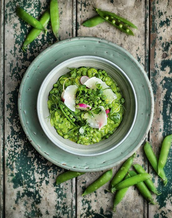 a bowl filled with green vegetables on top of a wooden table next to pea pods