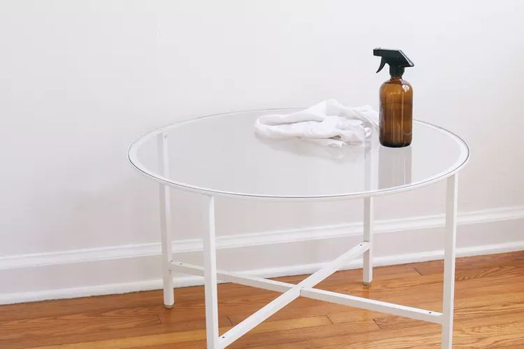 a spray bottle sitting on top of a glass table next to a white wall and wooden floor