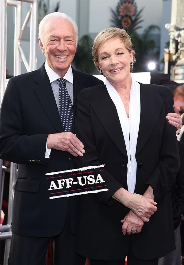 an older man and woman standing next to each other in front of a red carpet