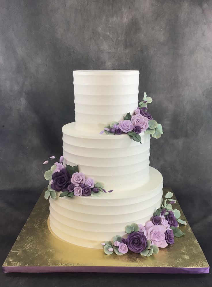 a three tiered white cake with purple flowers on the side and green leaves on top