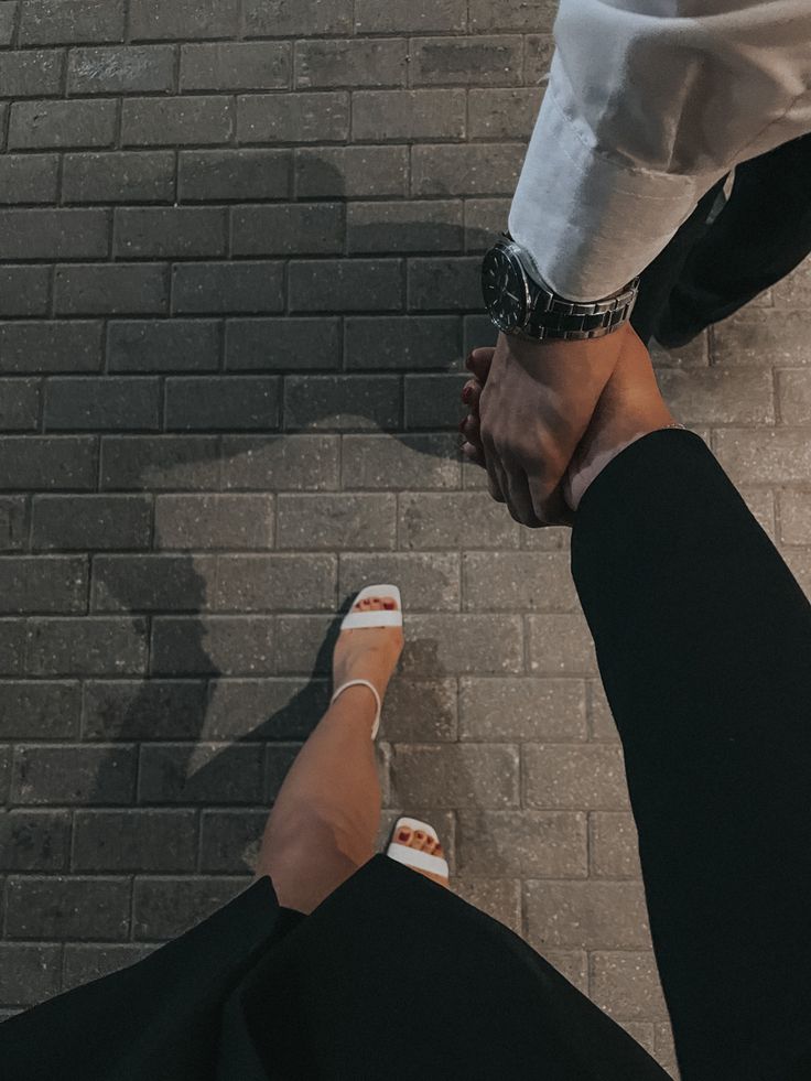 two people holding hands while standing next to each other on a brick wall and sidewalk