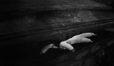 a hand reaching out from the bottom of a wooden beam in black and white photo