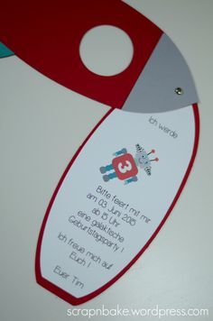 a close up of a red and gray rocket ship shaped birthday party card on a table