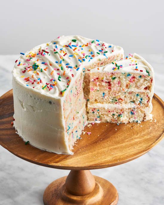 a cake with white frosting and sprinkles on a wooden plate