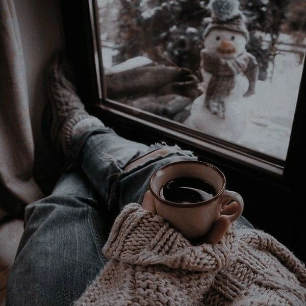 a person holding a cup of coffee in front of a snowman through a window