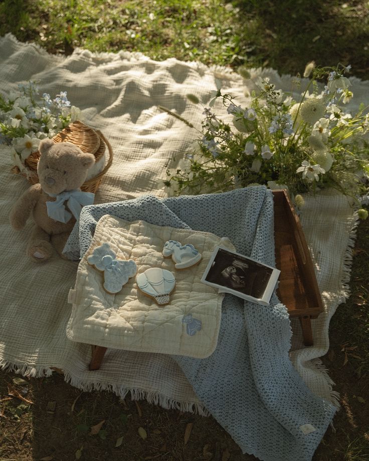 a teddy bear sitting on a blanket next to some flowers and an old photo frame