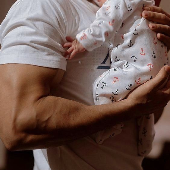 a man holding a baby in his arms and wearing a white shirt with anchors on it