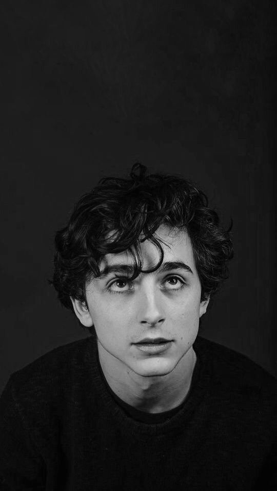 a black and white photo of a young man with curly hair looking at the camera