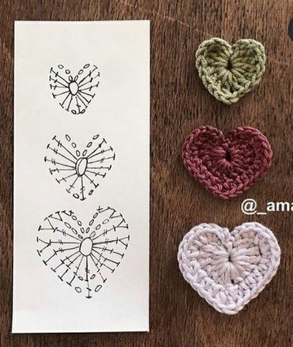 three crocheted hearts sitting on top of a wooden table next to a piece of paper