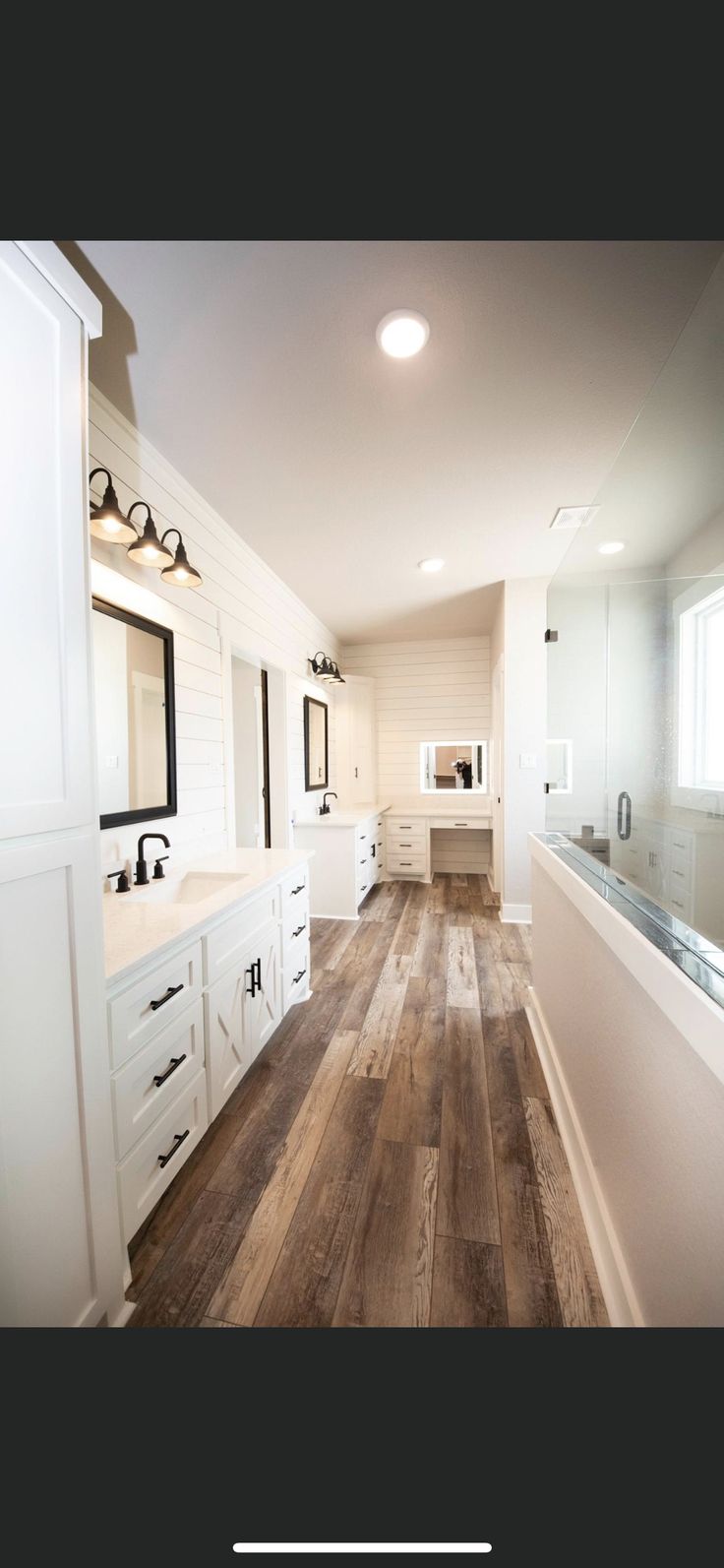 a large bathroom with wooden floors and white cabinets, along with mirrors on the wall