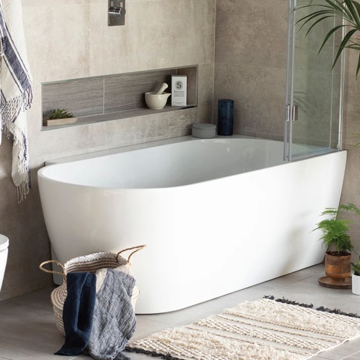 a white bathtub sitting next to a toilet and sink in a bathroom with potted plants on the floor