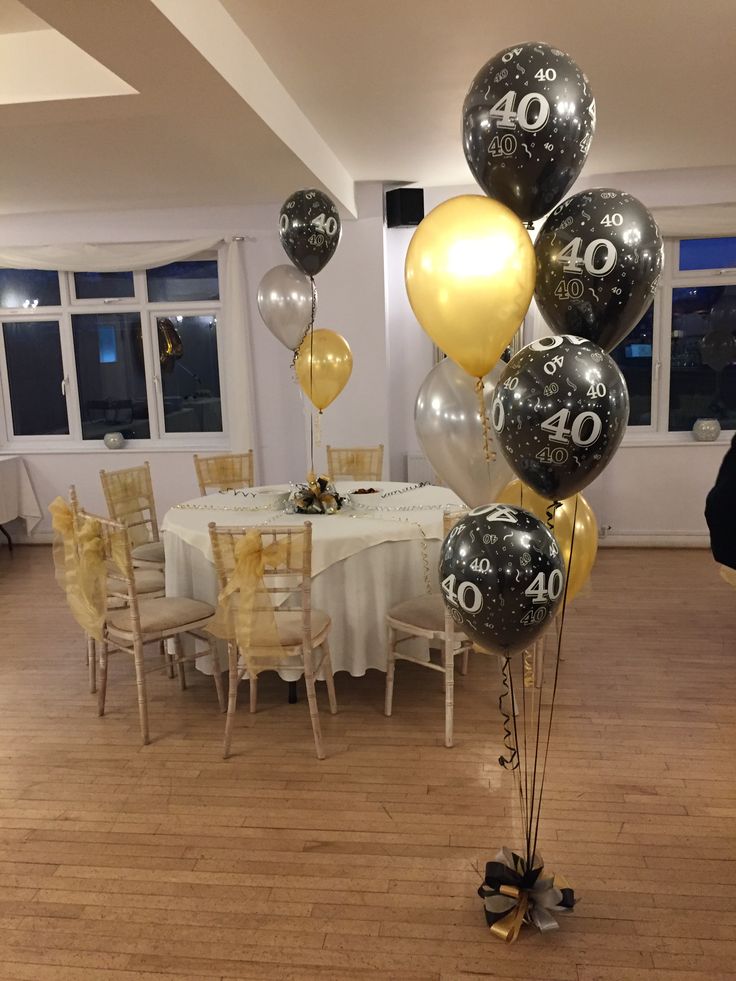 a room filled with tables and chairs covered in black and gold balloons that spell out the number forty