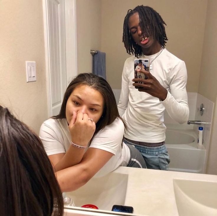 a man and woman looking at their cell phones in the bathroom while they are brushing their teeth