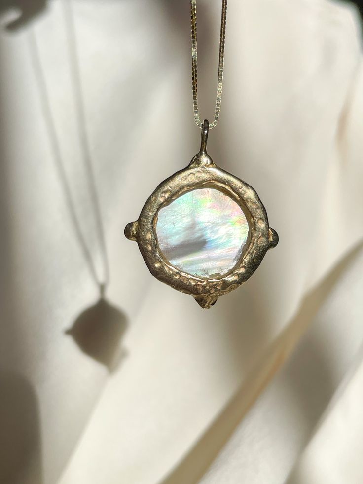 A dreamy 15mm hand-carved Mother of Pearl Moon encircled in gold, set with (4) White Diamonds, set on a solid 14k yellow gold 0.8mm box chain. (Approx. 5.7g.) Inspired in essence by the Impressionist French composer Claude Debussy, Clair de Lune translates to pale blue light or moonlight, and embodies the Divine Feminine energy of the moon, wholly encapsulating the deep sense of serenity found through inner self-awareness, and the strength kept within the gentleness of the heart. Aligns with int Celestial Yellow Gold Jewelry Gift, Celestial Style Yellow Gold Jewelry Gift, Celestial 14k Gold Round Pendant Jewelry, Heirloom Gold Jewelry With Pearl Pendant, Unique Round Pearl Pendant Jewelry, Recycled Gold Coin Pendant Jewelry Gift, White Gold Brass Jewelry With Round Shape, Moon-shaped Yellow Gold Brass Jewelry, Celestial Medallion Jewelry For Anniversary