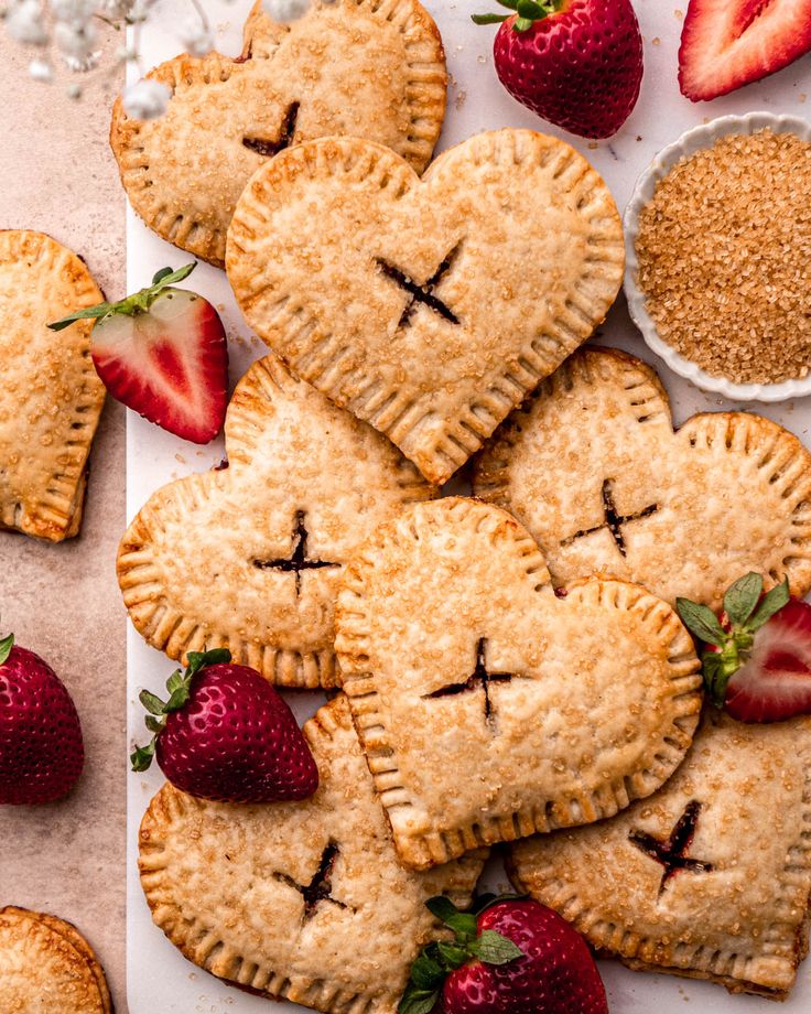 several heart shaped pies with faces drawn on them and strawberries next to it