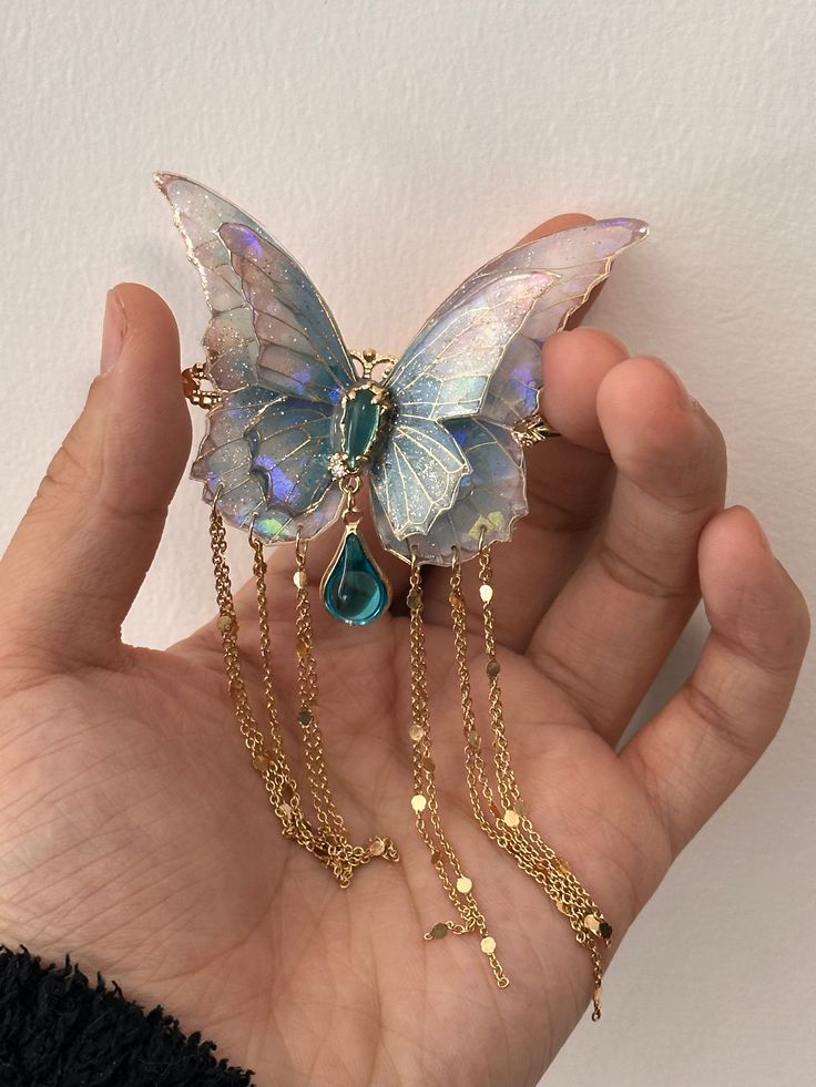 a hand holding a butterfly shaped brooch with chains attached to it's wings