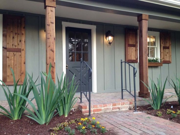 the front entrance to a house with wooden shutters and green plants on either side